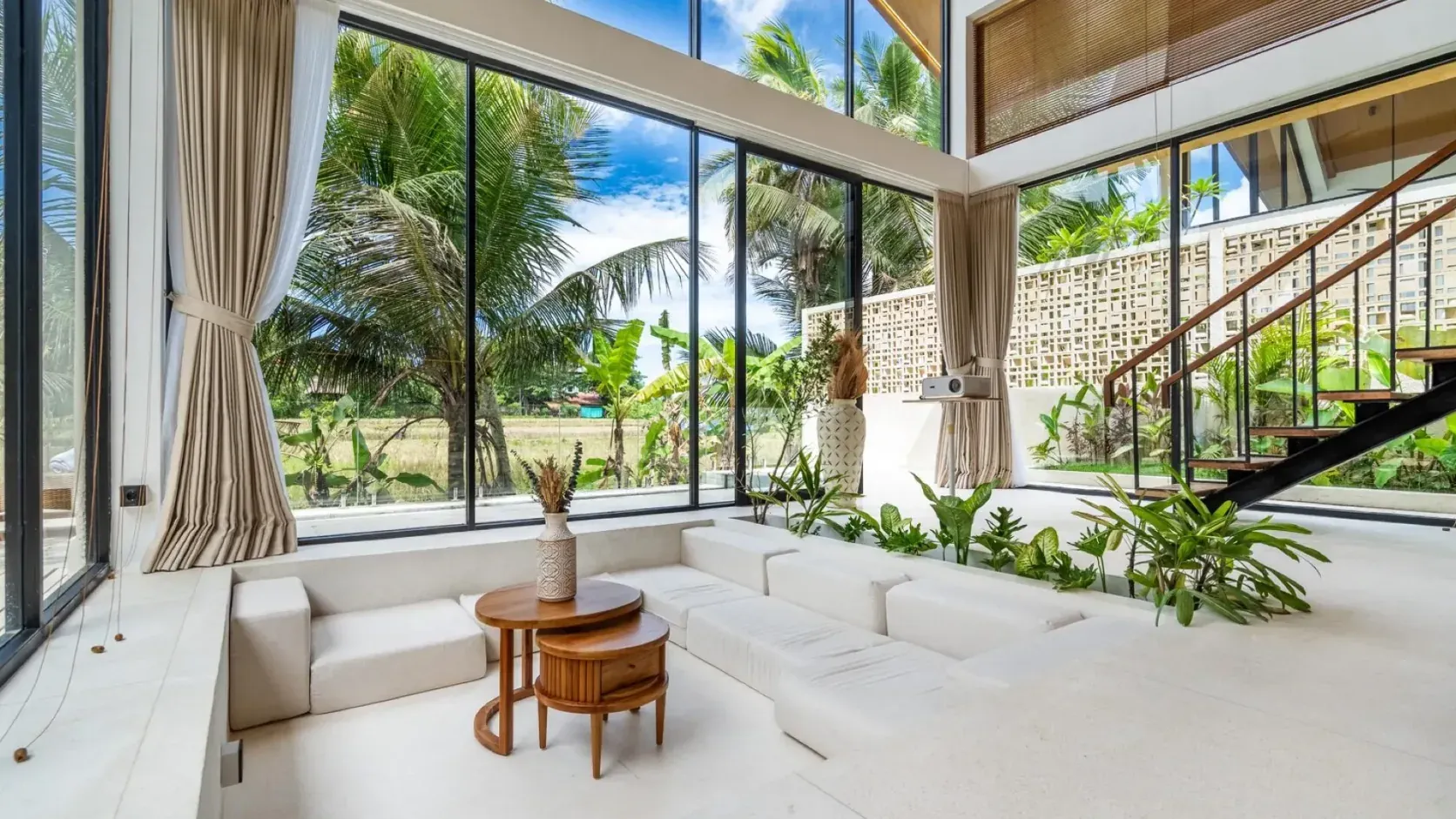 Double-height living room of a Dzen Green Fields villa in Ubud, with a low sunken sofa and floor-to-ceiling windows onto palms and rice fields