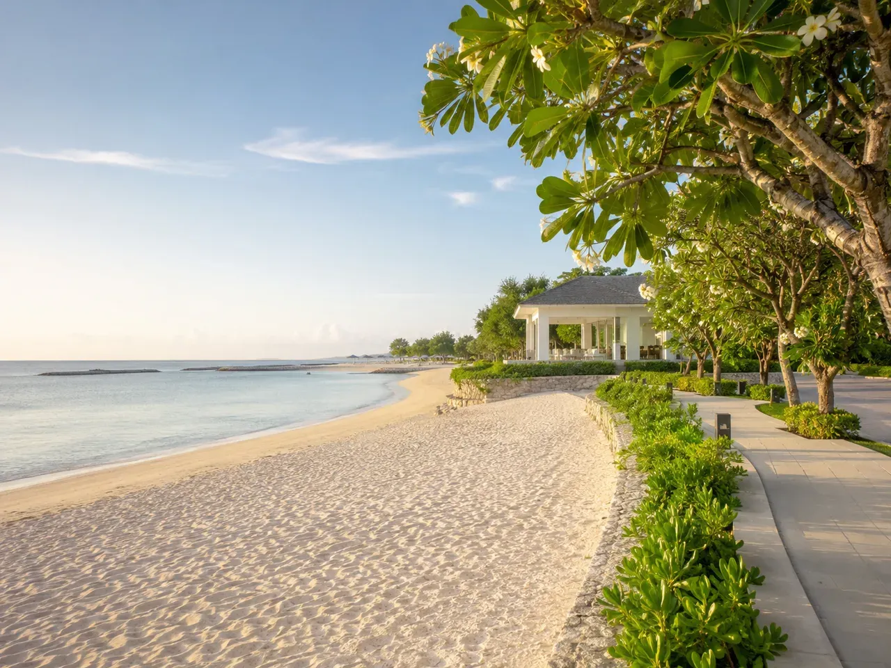 A calm reef-protected beach in Nusa Dua with a coastal walking path and frangipani trees
